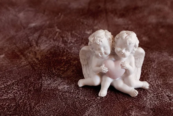 Kırmızı-kahverengi eski arka plan üzerinde ellerinde bir kalp ile sevimli beyaz meleklerin Heykelcik