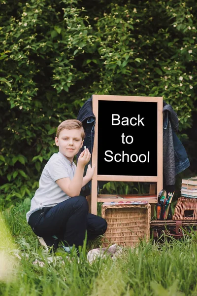 Back to school. Blonk happy schoolboy writes with chalk on blackboard. Place for text. Soft focus — Stock Photo, Image