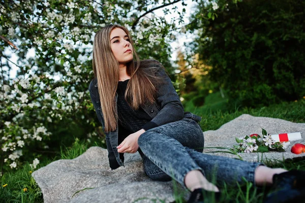 穿着牛仔裤的年轻黑发女孩坐在格子上对着春天的花朵树 — 图库照片