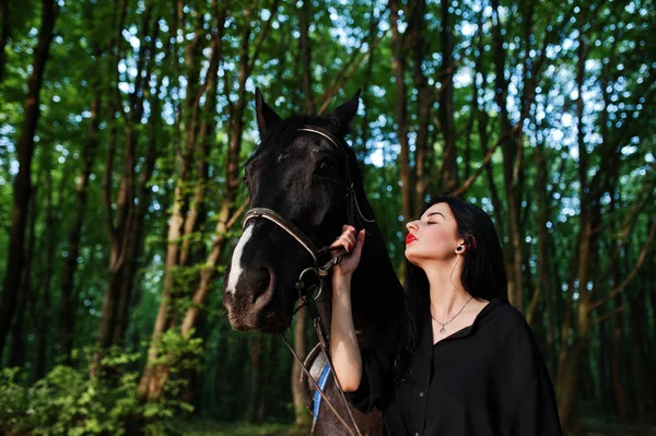 Mystical girl wear in black with horse in wood.