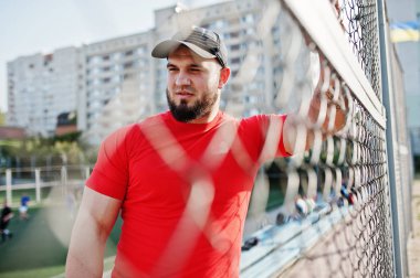Genç acımasız sakallı kaslı adam giymek kırmızı gömlek, şort ve cap adlı Stadyumu.