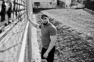 Genç acımasız sakallı kaslı adam giymek kırmızı gömlek, şort ve cap adlı Stadyumu.