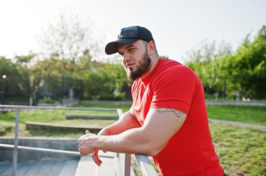 Genç acımasız sakallı kaslı adam giymek kırmızı gömlek, şort ve cap adlı Stadyumu.