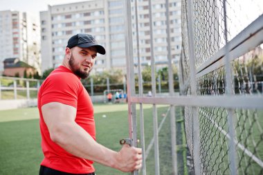 Genç acımasız sakallı kaslı adam giymek kırmızı gömlek, şort ve cap adlı Stadyumu.