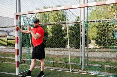 Genç acımasız sakallı kaslı adam giymek kırmızı gömlek, şort ve cap adlı Stadyumu.