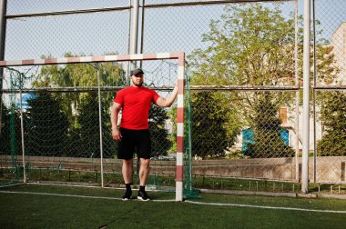 Genç acımasız sakallı kaslı adam giymek kırmızı gömlek, şort ve cap adlı Stadyumu.