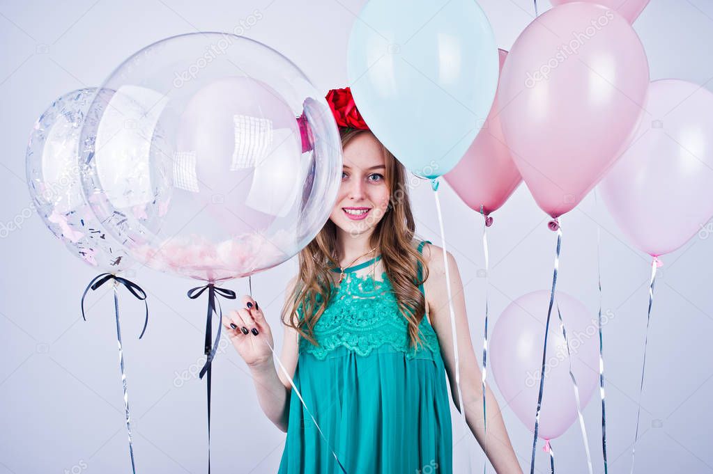 Happy girl in green turqoise dress and wreath with colored balloons isolated on white. Celebrating birthday theme.