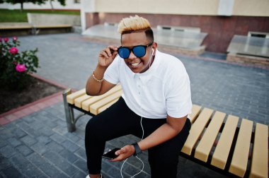 Aslında saç ve güneş gözlükleri şık Arap Müslüman çocuk sokaklarda, bankta oturan ve kulaklık telefonun müzik dinleme poz verdi.