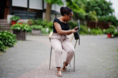 Şık Afrikalı-Amerikalı kadın güneş gözlüğü sandalyeye açık poz verdi.