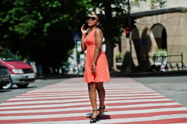 Yaya geçidi veya yaya geçidi üzerinde yürüme ve konuşma cep telefonu şık Afrikalı-Amerikalı kadın.