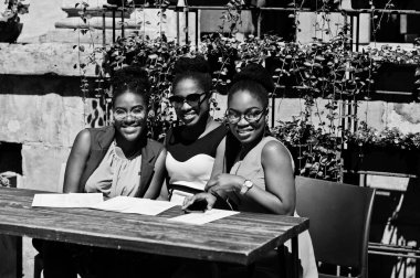 Güneşli yaz gün açık, elinde menüsüyle restoran masada oturan adlı üç şık Afrikalı-Amerikalı kadının poz.