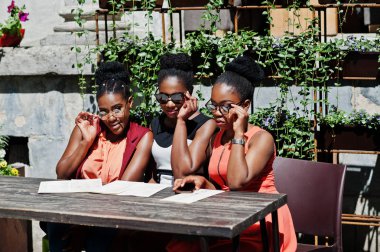 Güneşli yaz gün açık, elinde menüsüyle restoran masada oturan adlı üç şık Afrikalı-Amerikalı kadının poz.