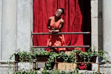 Şık Afrikalı-Amerikalı kadın, balkon kırmızı perde açık ile poz verdi.