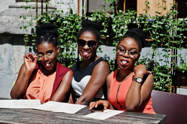 Güneşli yaz gün açık, elinde menüsüyle restoran masada oturan adlı üç şık Afrikalı-Amerikalı kadının poz.