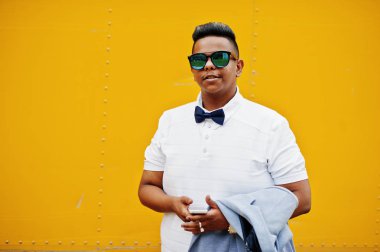 Güneş gözlüğü ve papyon cep telefonu ile sarı arka plana karşı yöneltilen şık Arap adam portresi kapatın. Arap modeli çocuk.