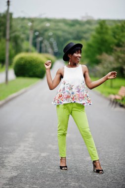 İnanılmaz bir Afro-Amerikan modeli kadın yeşil pantolon ve siyah şapka Park'ta farklı duygular ile poz verdi. 