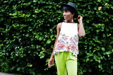 İnanılmaz bir Afro-Amerikan modeli kadın yeşil pantolon ve siyah şapka Park'ta farklı duygular ile poz verdi. 