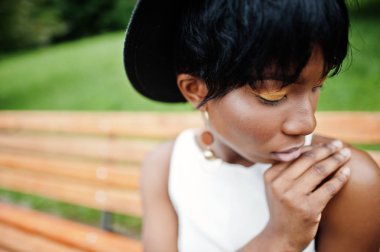 Yeşil pantolon ve siyah şapka parkta bankta yarattığı inanılmaz bir Afro-Amerikan modeli kadın. 