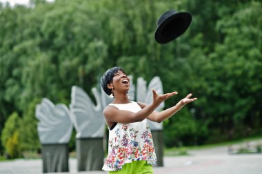 Afro-Amerikan model kadın yeşil pantolon içinde şaşırtıcı Park, hava atmak şapka poz verdi.