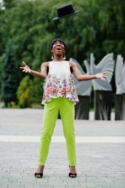 Afro-Amerikan model kadın yeşil pantolon içinde şaşırtıcı Park, hava atmak şapka poz verdi.