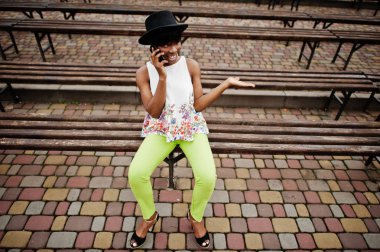 Afro-Amerikan model kadın yeşil pantolon ve siyah şapka tezgah yarattığı şaşırtıcı ve smartphone kullanarak.