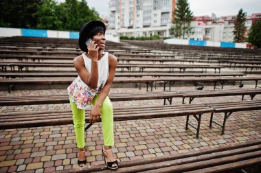 Afro-Amerikan model kadın yeşil pantolon ve siyah şapka tezgah yarattığı şaşırtıcı ve smartphone kullanarak.