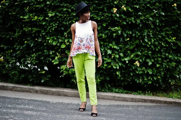 İnanılmaz bir Afro-Amerikan modeli kadın yeşil pantolon ve siyah şapka Park'ta farklı duygular ile poz verdi. 