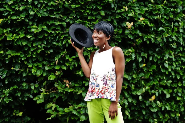 İnanılmaz bir Afro-Amerikan modeli kadın yeşil pantolon ve siyah şapka Park'ta farklı duygular ile poz verdi. 