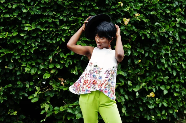 İnanılmaz bir Afro-Amerikan modeli kadın yeşil pantolon ve siyah şapka Park'ta farklı duygular ile poz verdi. 