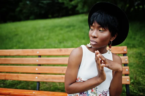 Yeşil pantolon ve siyah şapka parkta bankta yarattığı inanılmaz bir Afro-Amerikan modeli kadın. 