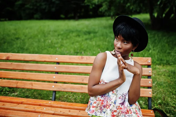 Yeşil pantolon ve siyah şapka parkta bankta yarattığı inanılmaz bir Afro-Amerikan modeli kadın. 