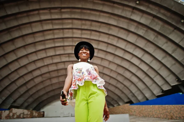 Afro-Amerikan model kadın yeşil pantolon ve siyah şapka şaşırtıcı arena hall karşı açık poz verdi.