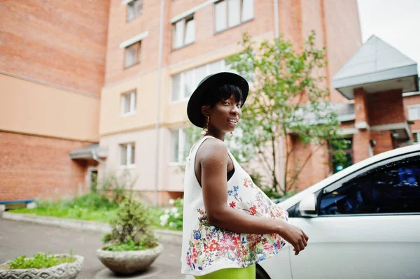 İnanılmaz bir Afro-Amerikan modeli kadın yeşil pantolon ve siyah şapka araba beyaz kapının yanında poz verdi.