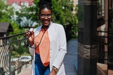 Afrika kökenli Amerikalı doktor erkek önlük, stetoskop ile gözlük, klinik karşı açık poz verdi.