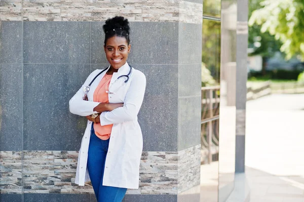 African american doctor female at lab coat with stethoscope posed outdoor against clinic.