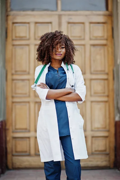African american doctor female at lab coat with stethoscope outdoor against clinic door.