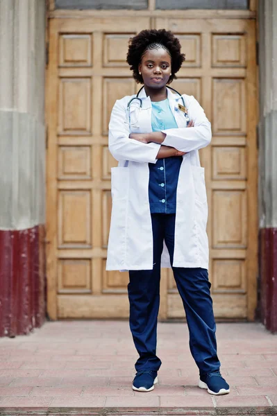 African american doctor female at lab coat with stethoscope outdoor against clinic door.