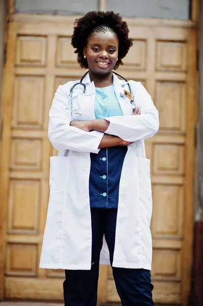 African american doctor female at lab coat with stethoscope outdoor against clinic door.