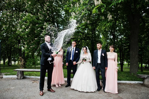 新郎の結婚式のカップルの公園とそばに立っている新郎と Braidsmaids のシャンパンのボトルを開く — ストック写真