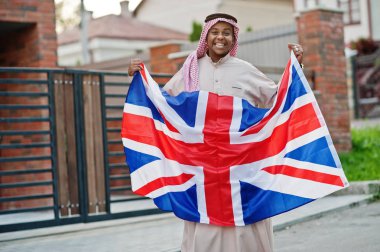 Middle Eastern arab man posed on street with Great Britain flag. England and Arabian countries concept. clipart