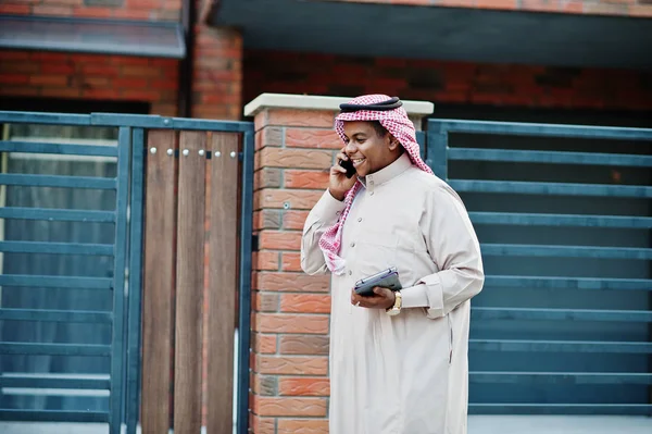 Orta Doğu Arap iş adamı tablet ve elinde cep telefonu ile modern bina karşı sokağında poz verdi.