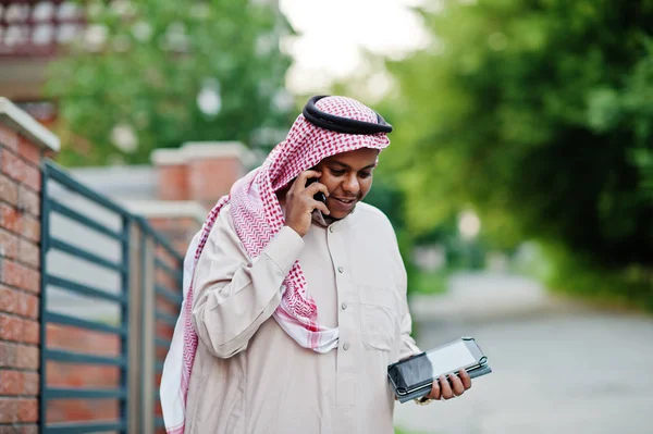 Orta Doğu Arap iş adamı tablet ve elinde cep telefonu ile modern bina karşı sokağında poz verdi.