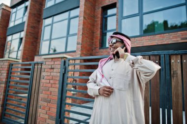 Güneş gözlüklü, modern bina karşı sokağında poz Orta Doğu Arap iş adamı üstünde hareket eden telefon konuşma.