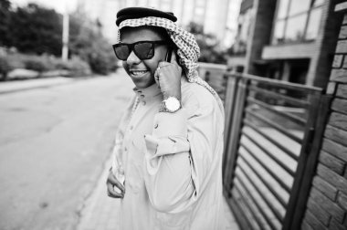 Güneş gözlüklü, modern bina karşı sokağında poz Orta Doğu Arap iş adamı üstünde hareket eden telefon konuşma.