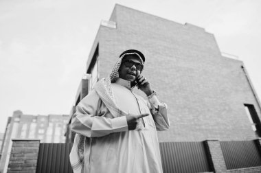 Güneş gözlüklü, modern bina karşı sokağında poz Orta Doğu Arap iş adamı üstünde hareket eden telefon konuşma.