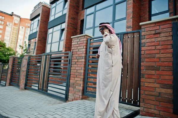 Middle Eastern arab business man posed on street against modern building with sunglasses, speaking on mobile phone.