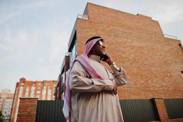 Güneş gözlüklü, modern bina karşı sokağında poz Orta Doğu Arap iş adamı üstünde hareket eden telefon konuşma.