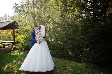 Mutlu yeni evli çift açık havada bahçe veya park ahşap gazebo yanındaki düğün gününde poz.