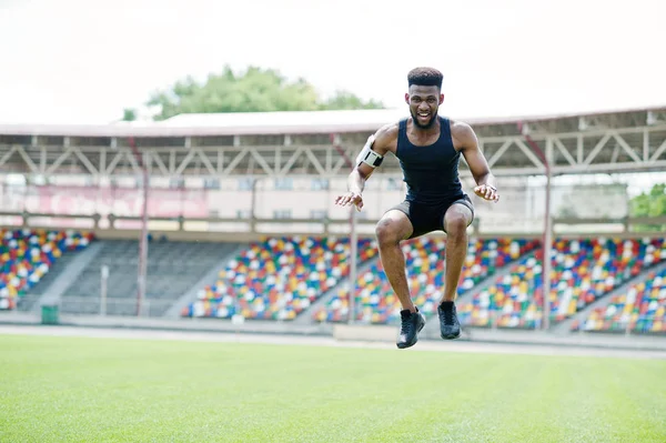 African american male athlete in sportswear doing jump exercise at stadium.