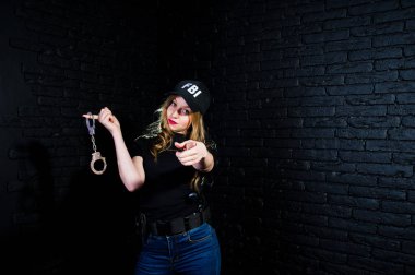 FBI kadın ajanı şapkalı ve karanlık duvara karşı stüdyoda silahla.